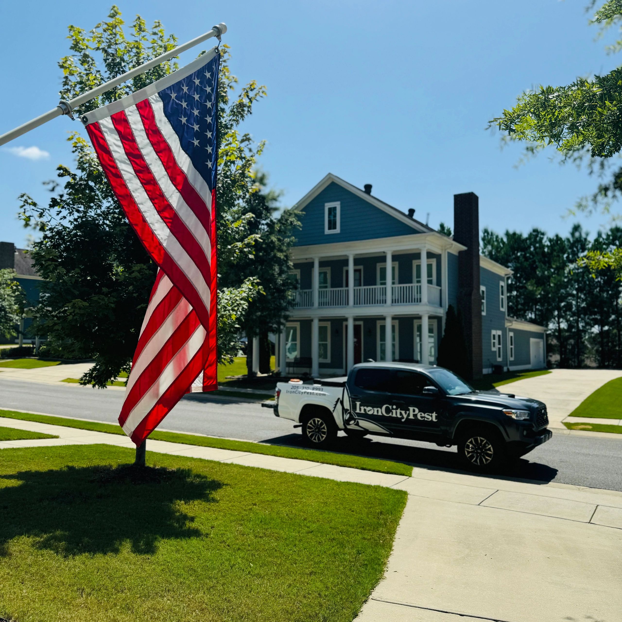 Iron City Pest Management's branded truck parked outside a flag-draped Birmingham-metro home